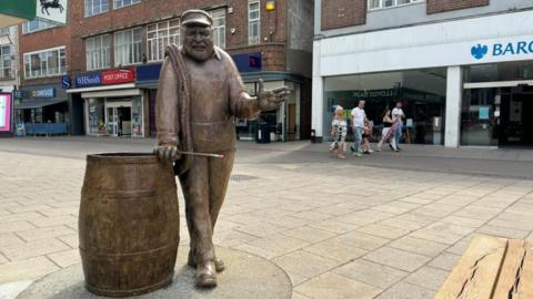 Yarn with Ernie, a bronze work in honour of local artist and potter Ernie Childs, installed in the Market Place. He is standing next to a barrel of herring.