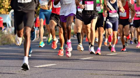 The legs of dozens of runners wearing running shorts and trainers during a running event