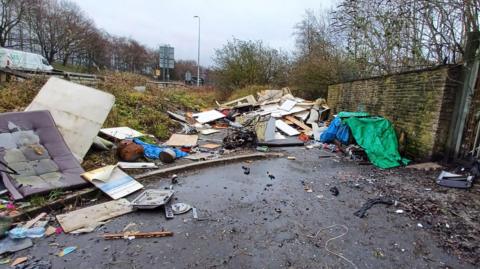 A temporary rubbish site on a grey road near a road strewn with rubbish and debris