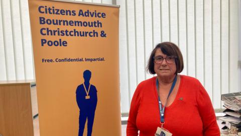 Zoe Bradley from Citizens Advice in her Bournemouth office. She is standing next to a Citizens Advice pop up banner.