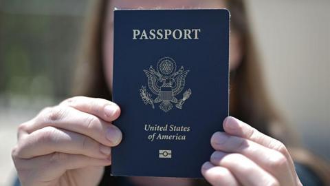 A woman holds up her US passport, blocking her face with it.