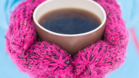 A person wearing mittens clasping a hot drink