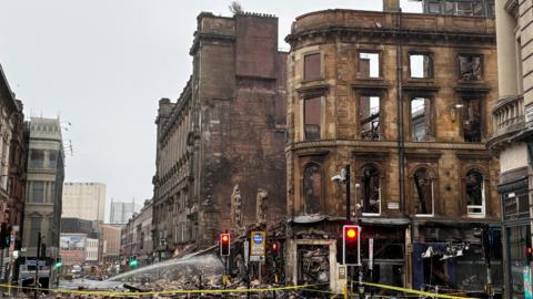 The remains of a building in Glasgow after the fire. A facade remains with nothing behind. The streets are covered in rubble and there is nobody in shot.