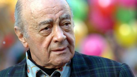 Close up head and shoulders portrait of Mohamed Al Fayed looking to the left of camera wearing a suit and shirt, with festive colouful balls out of focus in the background. Image taken at Harrods in London in 2007.