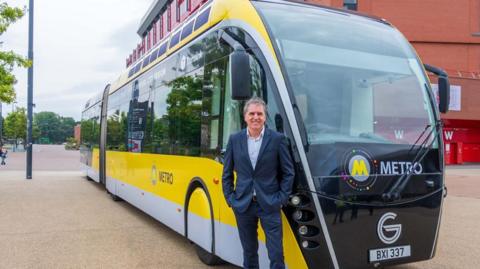 Metro Mayor Steve Rotheram stood in from of Glider bus which is parked outside Liverpool FC's Anfield Stadium