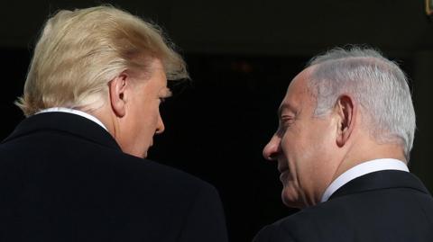 Trump is on the left with his back to the camera, looking right towards Netanyahu who is also with his back to the lens, looking left towards Trump. Both men have dark suits and white shirts