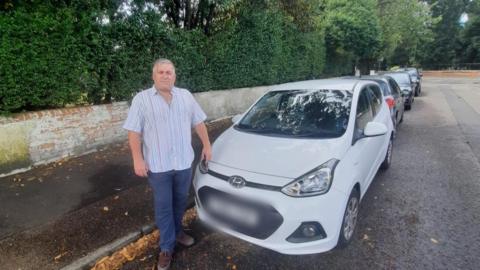 A man stands by a white parked car