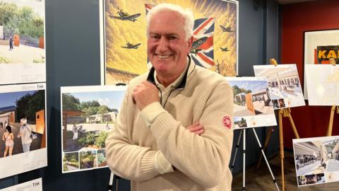 Lance Trevellyan smiling at the camera with architect images in the background at the War Tunnels.