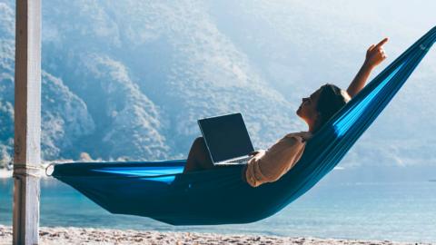A woman lounges on a hammock with a laptop in her lap