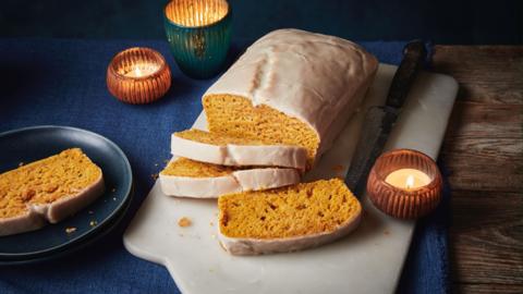 Iced loaf with some slices already cut sitting on a white chopping board