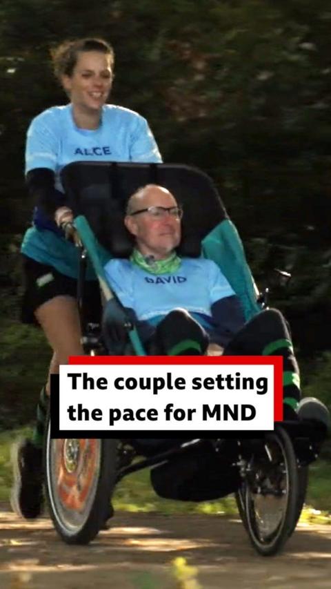 Alice is running behind a wheelchair which her husband David is sitting in