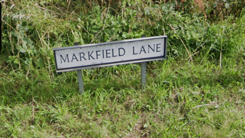 A street sign saying Markfield Lane with grass around the sign