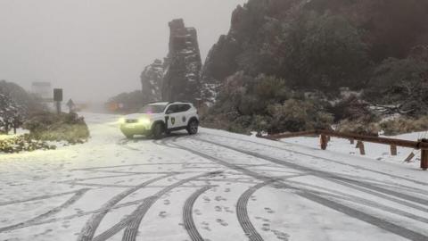 An emergency services car parked across a snow-covered rural road in fog