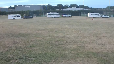 A CCTV image of three cars each towing caravans across a sports field.