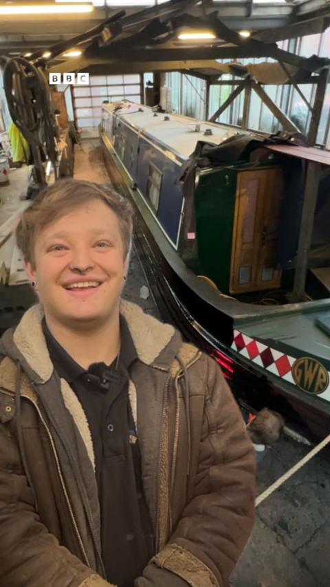 A ma stands in front of a canal boat.