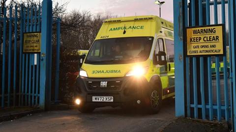 Photograph of ambulance being driven through blue gates.