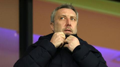 Jason Wilcox adjusts the collar of his coat while in the stands of a match