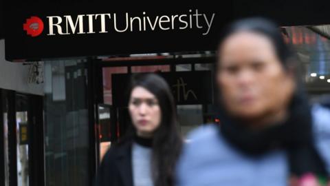 Women walk in front of an RMIT university sign