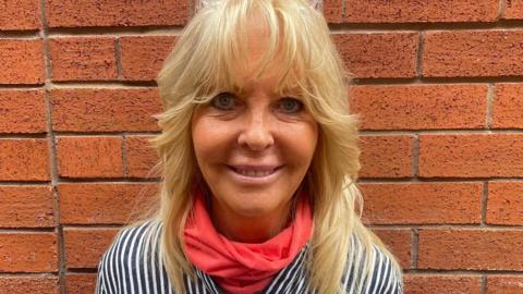 Mary Farnworth smiling wearing an orange scarf and black and white striped shirt