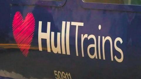 A close-up of the side of a dark blue train carriage with a large logo reading "Hull Trains" in white text, next to a pink heart. A train serial number reads "50911".