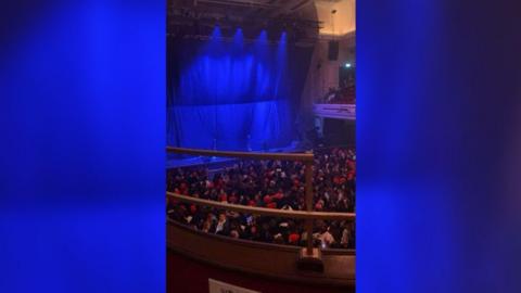 The O2 City Hall Newcastle photographed from the balcony ahead of Zayn Malik's concert. The stage curtains are in place and lit up in blue. The floor below is packed with people. 