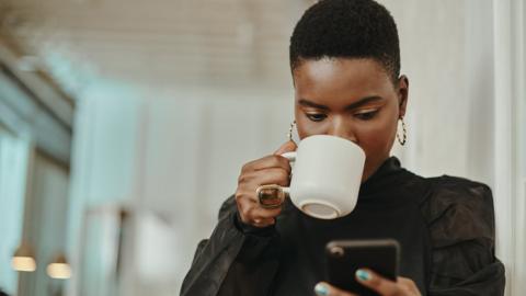 Woman drinking a hot drink and looking at her phone