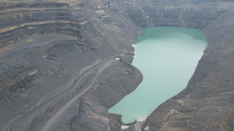 An aerial photograph of water pooling in the main void at Ffos-y-Fran mine. The water is bright blue, while grey cliffs walls surround it. 