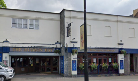 The former Hudson Bay pub with a bus stop and shelter in front of the venue and a church spire in the background 