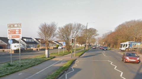 A red car drives alongside Westgate in Morecambe, with a lorry behind about to turn into the road