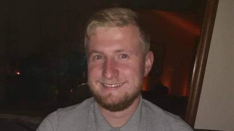 Jack Bristow is smiling broadly at the camera. He has fair hair and a beard and wears a grey shirt.