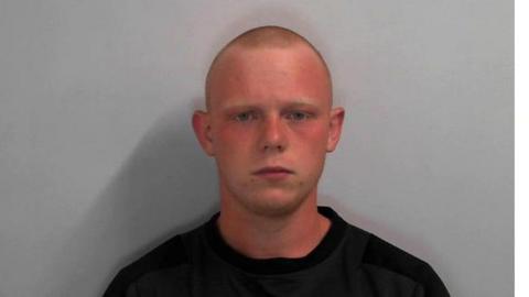 A mugshot of James Martin, who has a shaven head, and is wearing a black top.