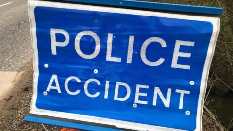 A blue "Police accident" sign on the verge of a road.