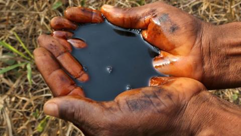 A man holds a pool of black oil in the palm of their hands in Ogoniland, Nigeria