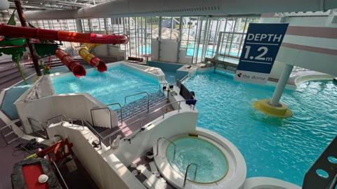 A leisure centre swimming pool area with slides, a jacuzzi and large pool