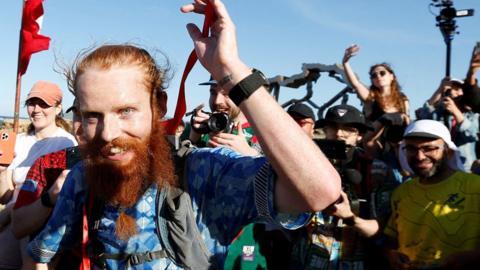 Russell Cook gestures and smiles while crossing the finishing line of his Africa run on 7 April