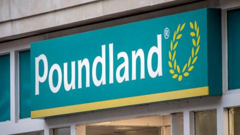 Turquoise shop sign which reads 'Poundland' in white letters with a yellow wreath. 