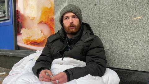 Jaden Forrest, a homeless man in Leeds sat outside a shop with a white duvet 