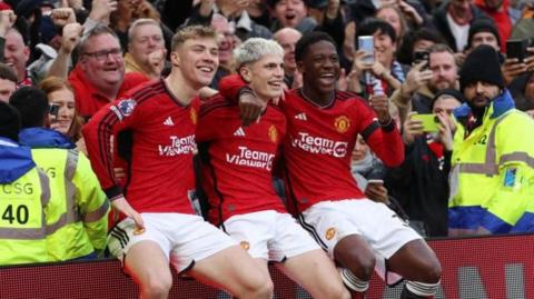 Rasmus Hojlund, Alejandro Garnacho and Kobbie Mainoo sitting on the advertising boards at Old Trafford