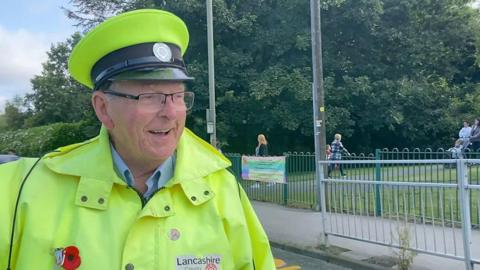 Lollipop man Arthur Parker in his uniform smiling outside a school