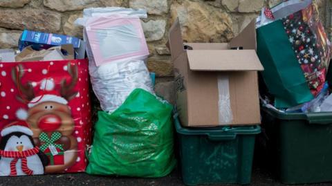 Rubbish left out for bin collections - includes brown boxes, a festive large red gift bag and green plastic trays containing more waste