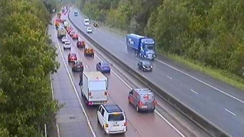 An overhead view of a motorway, where the closest side to the camera is heavily congested with traffic.