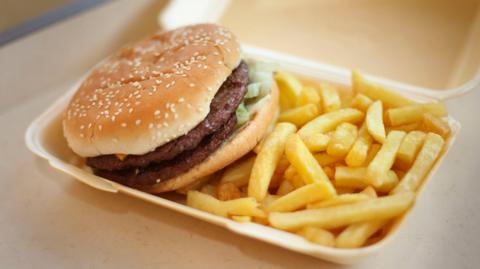 Generic image of a double burger in a bun with sesame seeds and fries in a take away carton. 