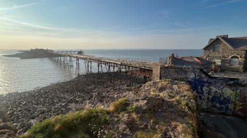 A view of Birnbeck Pier with the tide out. The pier is derelict, as are the buildings near it