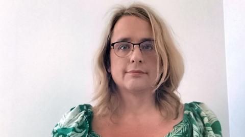 Emma Harris wearing glasses and a green floral top against a white wall