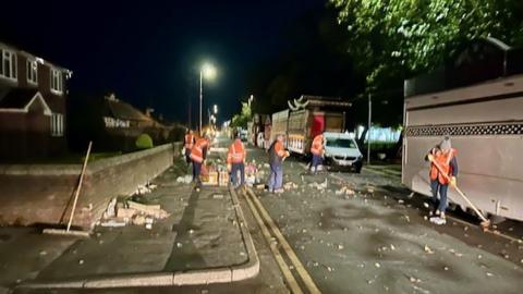 Council workers in orange high visibility jackets sweep the streets around the fair stalls at night