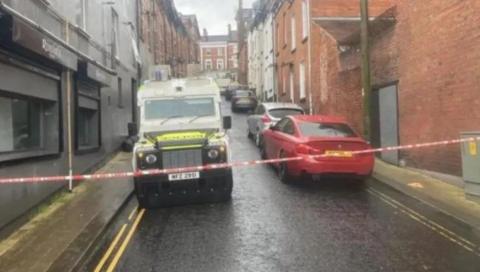 Shows a police Land Rover and cordon 