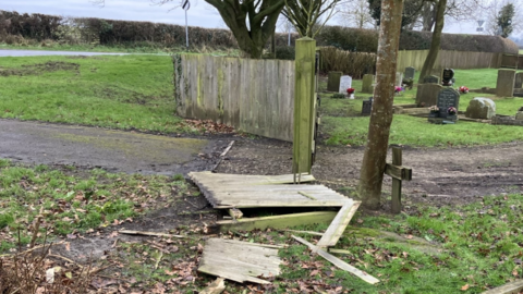 A smashed fence in front of some gravestones