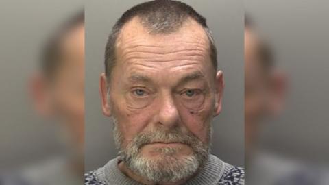 Police custody photograph of Dale Bryan Halliday who has dark hair and a grey beard and is wearing a grey jumper.
