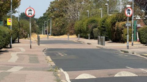 A general view of Pathfields Road, which has traffic calming measures including speed bumps. There is a pathway lined with trees at the end.