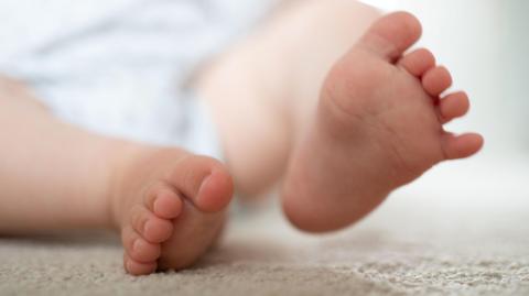 Close-up of two small bare feet resting on a soft, light-colored surface, with toes slightly curled and background softly blurred